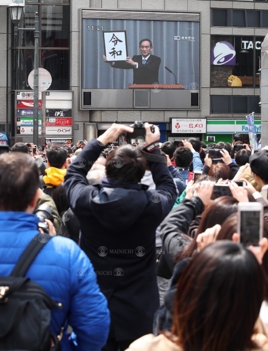 People taking pictures of a large monitor showing Chief Cabinet Secretary Yoshihide Suga s press conference announcing the new name of Japan,  2019. People take photos of a large monitor showing Chief Cabinet Secretary Yoshihide Suga s press conference announcing the new name of the Japanese government,  2019  Heisei 301 ,  in Chuo Ward, Osaka City, April 1, 2019. Photo by Maiko Umeda at 11:41 a.m. on April 1, 2019 in Chuo Ward, Osaka City.
