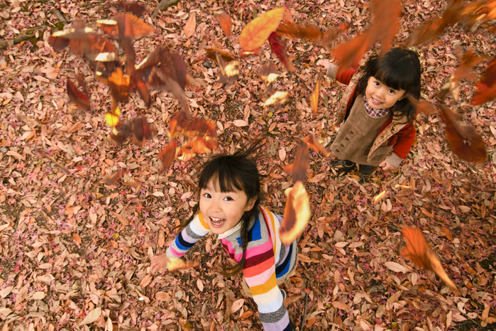 Girl throwing fallen leaves in park with autumn leaves