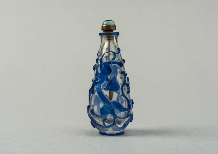 Clear glass snuff bottle with blue overlay, China, Qing dynasty, 1644 1911. Creator: Unknown. Clear glass snuff bottle with blue overlay, China, Qing dynasty, 1644 1911. Glass snuff bottle of elongated tear drop form. Clear body with dark blue applied decoration of stylised animal motifs on either side  dragon and tiger. Gold shaft, spoon and mount for pale blue stone.