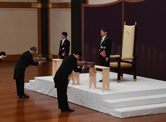 The new Emperor of Japan at the  Sword and Seal Succession Ceremony. In the foreground, a chamberlain places the sword and regalia, the  Three Sacred Treasures,  on the proposed succession ceremony. The new Emperor of Japan at the  Succeeding Ceremony of the Sword and the Seal . In the foreground is a chamberlain placing the sword and regalia, the  Three Sacred Treasures,  on a draft.