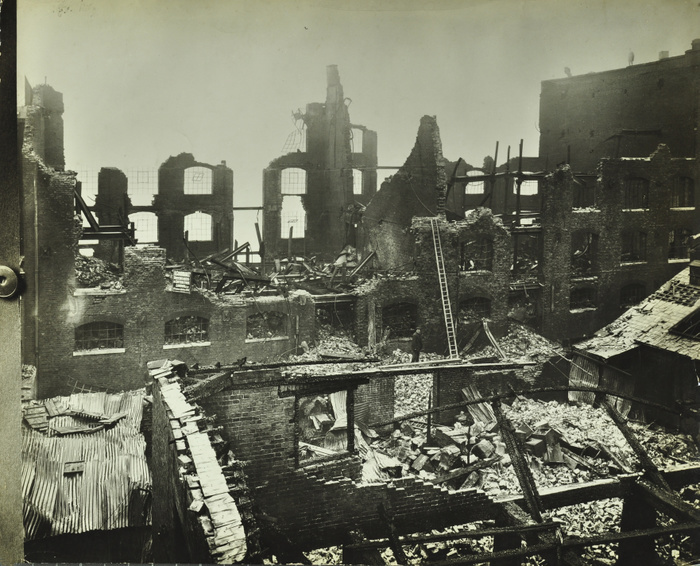 Burnt-out building, Concordia Wharf, Poplar, London, 1924. Shell of a warehouse revealing the interior with rubble and wreckage after a fire. Roofs have been destroyed, windows blown in and walls fallen down. Ladder and officer are shown.