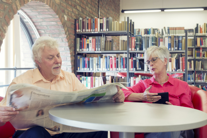 Senior Male Senior couple with newspaper and e book in a city library