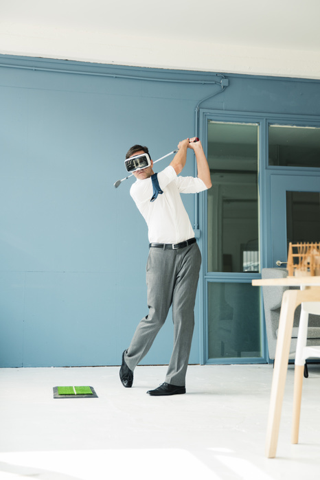 Businessman wearing VR glasses playing golf in office Businessman wearing VR glasses playing golf in office