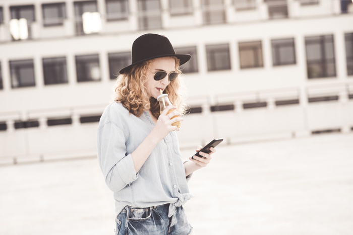 female Young woman drinking beverage while using cell phone
