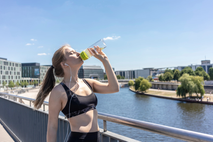Young woman taking break from exercise and drinking water in city, Berlin, Germany