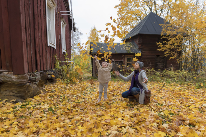 Finland, Kuopio, mother and little daughter throwing autumn leaves in the air Finland, Kuopio, mother and little daughter throwing autumn leaves in the air