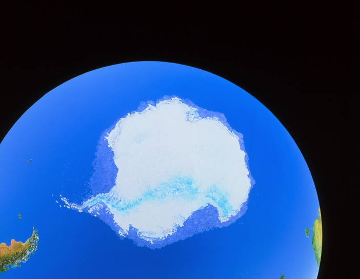 Image of the Antarctic continent. Antarctica is seen here with its white permanent ice cap. Surrounding it is a slightly pale blue colour indicating the average extent of Antarctic sea ice. The largest areas of sea ice are the Ronne Ice Shelf (left coast) and the Ross Ice Shelf (bottom right coast). The southern tip of South America is seen at bottom left, and the southern extent of Australia at bottom right. The bright blue streak across the continent represents the Transantarctic Mountain range. This photograph is a simulation of space-based imagery.