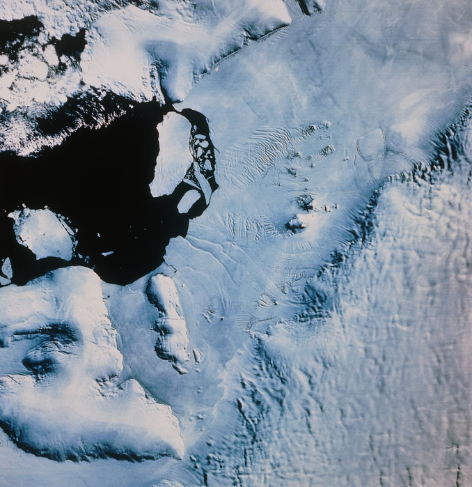 The English Coast of Antarctica, imaged by Landsat 1 on 9 January 1973. The region in lower right is Palmer Land at the base of the Antarctic Peninsula. At bottom left, Spaatz Island is seen rising above the ice shelf, whilst the edge of Alexander Island is seen at top centre. The relatively flat ice shelf running diagonally across the frame covers George VI Sound, whilst at top left is the bare surface of water in the Ronne Entrance. This image was made in the Antarctic summer, so the ice cover is at a minimum. The iceberg seen toward top left of centre is about 35km long.