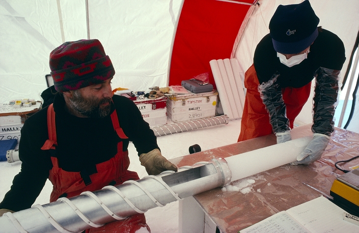 Climate change research. Atmospheric scientists removing an ice core taken from the Antarctic Peninsula. The air trapped in the firn (the upper layer of frozen snow) is untainted by the atmospheric air, and thus provides direct evidence of what the composition of the atmosphere was at the time when the firn froze. This research was done as part of the EPICA project (European Project for Ice Coring in Antarctica). Studying how the atmosphere has changed can lead to better models for predicting how it will change in the future. Photographed in Dronning Maud Land, Antarctica.