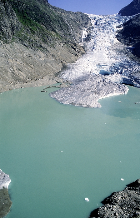 Glacial retreat. Image 2 of 2. Terminus of the Triftgletscher glacier, Switzerland, in August 2003. A glacier is a river of ice that flows down from mountain areas. The ice forms from compacted snowfall, and erodes the rock underneath it as it moves forward. The position of the terminal end of the glacier depends on the rate of melting at the terminus, versus the rate of snowfall further up the glacier. The melting forms the glacial lake seen here, which first started to form in 2001. Since 1850, glaciers have been in retreat worldwide. It is thought that global warming has accelerated this trend in recent years. See E235/340 for this glacier in 2002.