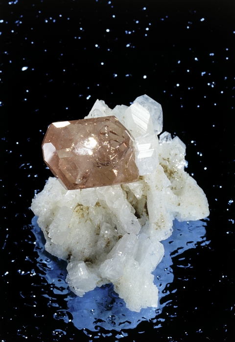 A crystal of pink apatite growing on an aggregate of albite crystals. The name apatite refers to a number of minerals of different compositions, including various metal phosphates, arsenates and vanadates. Albite (sodium aluminium silicate) is colourless or white and forms two different types of crystal; the prismatic variety seen here (known as pericline) and a lamellar (plate-like) variety (known as cleavelandite). This specimen measures 3.5 x 2.5 cm and was found in Itatiaia's Mine, Conselheiro Pena, Brazil.
