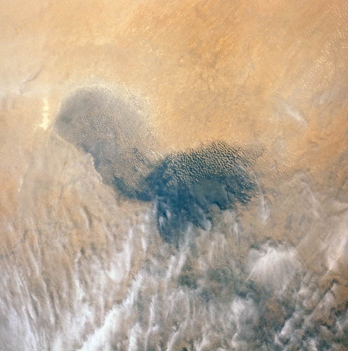 Shuttle picture of Lake Chad (central grey area). North is at top. The fluctuating water level of the lake is an environmental index of drought in north-central Africa. The lake level is decreasing, as is shown by the sand dunes north of the lake, which were previously submerged. Some of the dunes still trap a little water. Of all the world's inland bodies of water Lake Chad is perhaps the most frequently-photographed subject for cameras in orbit, hence the reduction in its size, which has occurred over the past two decades, is well documented. The clouds in the area are not of the type which produce rain.