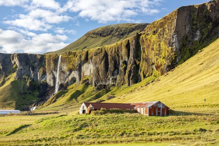 Farm buildings by Foss a Sidu waterfall, Iceland Farm buildings by Foss a Sidu waterfall, Iceland. The waterfall  background left  is part of the Fossa river. It is 30 metres tall and is surrounded by basalt rock. Photographed in September 2018, on the road from Kirkjubaejarklaustur to Skaftafell, Iceland.