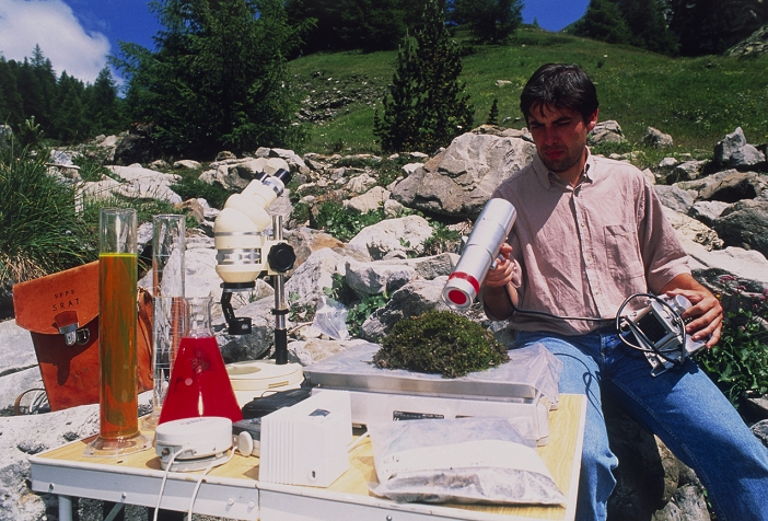 Radioactivity analysis. Researcher using a geiger counter to measure the radioactivity levels of moss gathered from a mountainside. Part of the Geiger counter is a tube filled with low pressure gas. As radiation passes through the tube it ionises (charges) the gas particles. The number of charged particles and hence the radiation level is recorded on a dial. Among the items on the table is a microscope. This work is being carried out by the French government agency, l'Institut de Protection et de Secrete Nucleaire (ISPN). Photographed at the Mercantour Mountains in the French Alps.