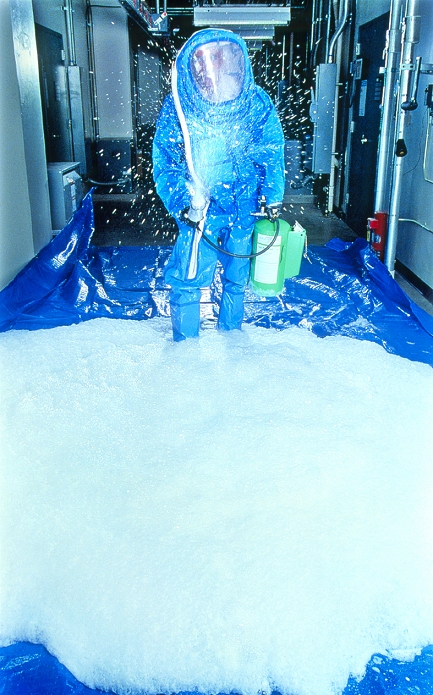 Decontamination foam testing. View of a researcher spraying decontamination foam in a laboratory. In minutes, this foam neutralises biological and chemical weapons such as anthrax bacteria, viruses and VX nerve gas. It is intended to be the first line of defence against an attack or accident, even before the emergency personnel know what they are dealing with. The foam is harmless to humans, and can be sprayed before any evacuation has taken place. It is a combination of detergents and oxidising agents, which work together to render the agents harmless. It is being developed at Sandia National Laboratories in the USA.