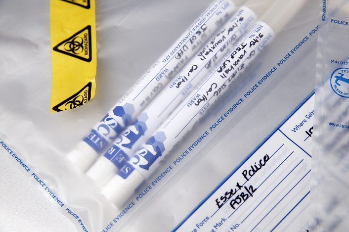 Forensic evidence. Police evidence bag containing three swab sample containers. The samples have been taken from a motorist by a scene of crime officer (SOCO). Biohazard warning tape has been stuck to the bag. A person found guilty of an offence by the police has to supply a saliva sample. From this a DNA profile can be formed and compared to profiles already held on the National DNA Database (NDNAD). The NDNAD was set up by the Forensic Science Service in 1995.