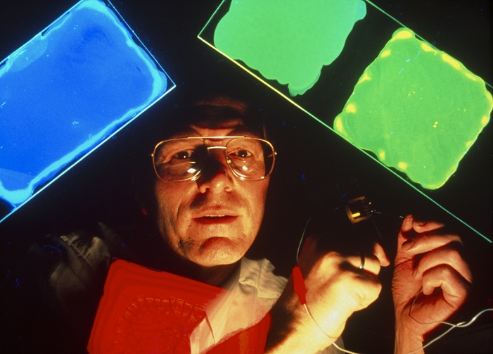 Dr Andrew Holmes holds in his hands a tiny sample of a light-emitting plastic, which is emitting a gold glow. In this photomontage, he is surrounded by close-ups of the same plastics emitting green, blue and red glows - the 3 colours needed to make a colour TV image. Light-emitting plastics - such as polyphenylene vinylene (PPV) - are polymers which emit light when a voltage is set up across them. They were discovered in 1990 by Dr Richard Friend and Dr Donal Bradley of the Department of Physics at the University of Cambridge, UK, and Dr Holmes of the Department of Chemistry. The plastics could be used in applications like LEDs (light-emitting devices) and thin-screen TVs.