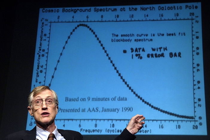 Dr John Cromwell Mather (born 1945), American astrophysicist, cosmologist and Nobel laureate, talking at a press conference about the work for which he was awarded a share of the 2006 Nobel Prize in Physics. The graph in the background presents data from the COBE (Cosmic Background Explorer) probe, which was launched in 1989. This probe measured the cosmic background radiation, a microwave radiation that permeates the entire universe, and is one of the strongest pieces of evidence for the Big Bang theory of the origin of the universe. Mather's COBE work helped show the black body nature of the radiation (as shown by the graph). Photographed at NASA Headquarters, Washington DC, USA, on 3 October 2006.