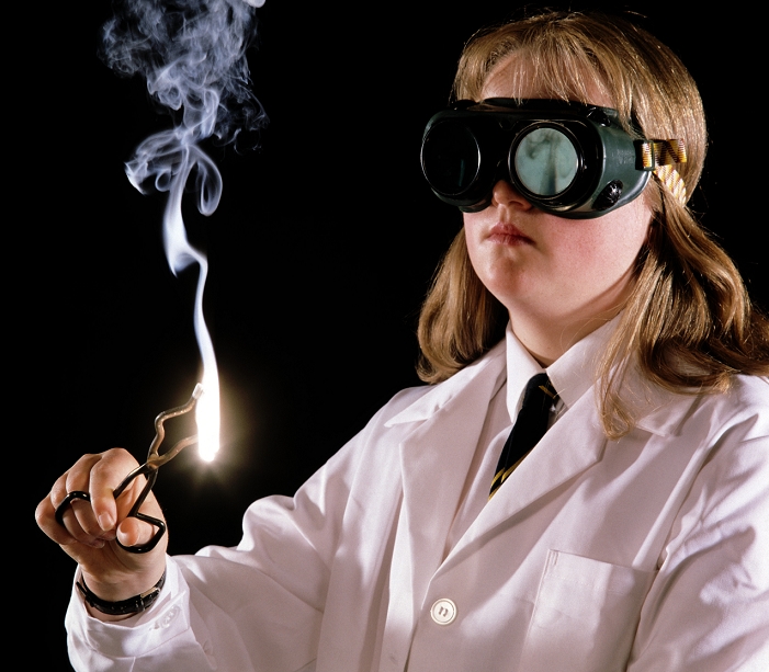 . Burning magnesium. Schoolgirl burning a piece of magnesium ribbon during a chemistry lesson. She is using tongs to hold the burning magnesium and wearing safety goggles to protect her eyes from the glare of the white flame. Magnesium will readily burn in air to produce magnesium oxide. MODEL RELEASED