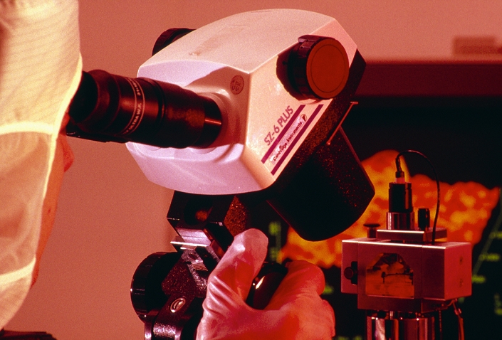 A researcher setting up an atomic force microscope (AFM), ready for use. A binocular light microscope is used to ensure that the AFM probe is in the correct starting place on the sample. The AFM is capable of atomic-scale resolution, and works by drawing a very fine 'stylus' across the surface of the sample. A carefully-balanced spring ensures that the tip follows the contours of the sample, enabling a map to be constructed of its surface. The AFM is similar in concept to the slightly more powerful scanning tunnelling microscope (STM), but has the advantage that it may be used with non- conductive samples such as biological specimens.