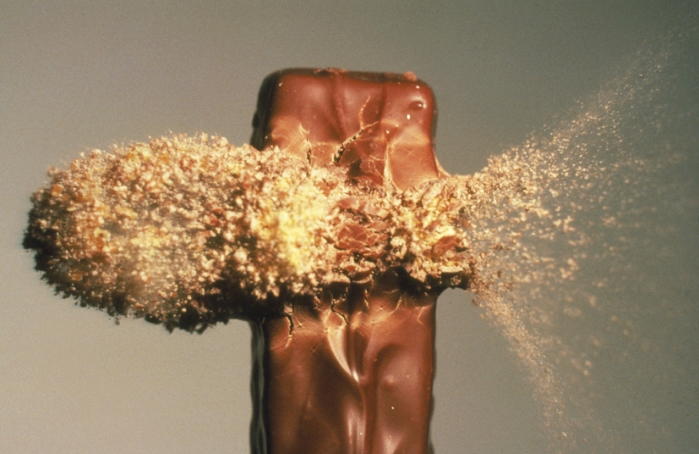 High speed photograph of a . 22 calibre bullet hitting a chocolate bar. The bullet, emerging in a cloud of fragments, is travelling at about 450 metres per second (Mach 1.4).