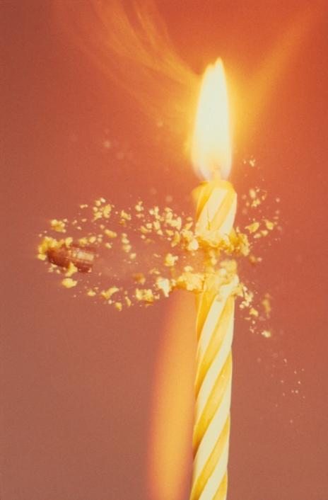 High speed photograph of a . 22 calibre bullet striking a burning candle. The bullet, emerging in a shower of wax fragments, is travelling at about 450 metres per second (Mach 1. 4). The bright streak to the left of the candle was caused by the candle flame as the upper part of the candle fell away after the impact.