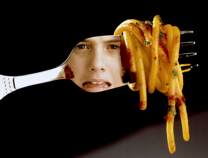 . Anorexia nervosa. Girl's fearful face reflected in a fork which has a twirl of spaghetti on it. Her anxious look reflects her fear of eating and gaining weight. This fear of becoming fat characterizes the eating disorder anorexia nervosa (or 'slimmers disease'). Such obsessional fear leads to the avoidance of food and consequent severe weight loss. Sufferers are overactive, and exercise much of the time. As they lose weight they become tired, weak, their hair thins and the menstrual cycle may cease. Food binges may be followed by vomiting or taking laxative drugs. Teenage girls and young women are most often affected. MODEL RELEASED