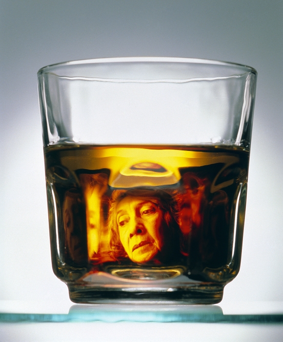. Alcohol addiction. Glass of alcohol, with an abstract image of a woman reflected in the liquid. In her expression, the woman appears to be struggling with her addiction. Alcohol is an addictive substance which acts as a depressant on the nervous system, and so reduces anxiety, tension and inhibitions. Dependency on alcohol (alcoholism) is an illness which leads to withdrawal symptoms when drinking is suddenly stopped. Long term and excessive alcohol consumption may cause irreversible damage to the heart, liver, brain and nervous system. MODEL RELEASED