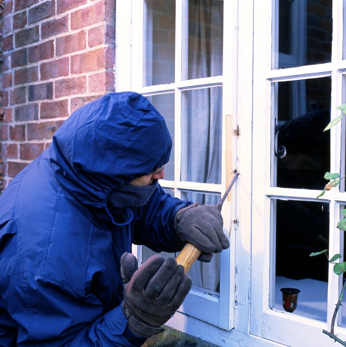 Burglary. A masked and hooded man levers open a window in order to perpetrate a burglary.