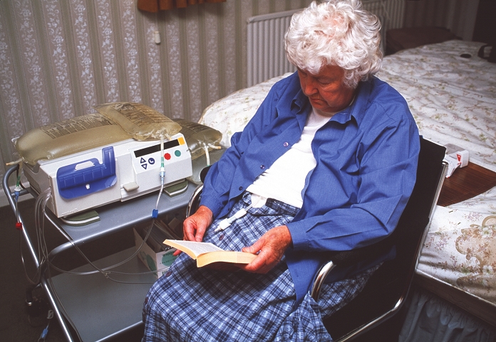. Kidney dialysis. 70-year-old woman reading a book at home during peritoneal dialysis. Dialysis carries out the normal function of a failing or failed kidney, to remove waste products from the blood. In peritoneal dialysis, the filter used is the patient's own peritoneum (abdominal lining). The dialysis fluid (bags at upper right) enters the abdominal cavity via a catheter (lower centre). Waste products from the blood pass across the peritoneum to accumulate in this fluid, which is then drained and replaced. The feasibility of this dialysis method depends upon factors such as the patient's remaining kidney function, abdominal capacity and the quality of their peritoneum. MODEL RELEASED