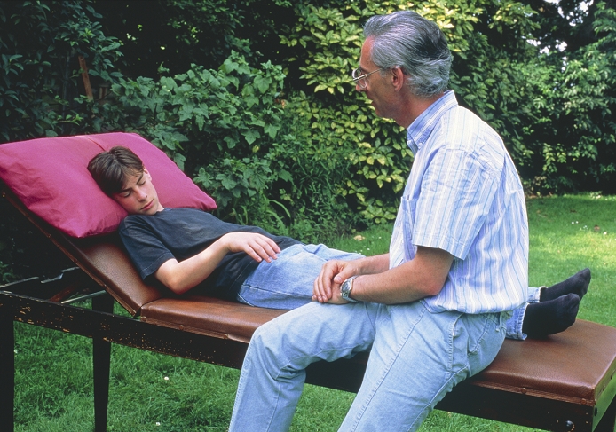 A hypnotherapist with a young subject. Hypnosis is a trance-like state, characterised by extreme Suggestibility. Here the hypnotherapist has suggested to the subject that he has a balloon tied to his right hand. The subject's right arm has raised accordingly. Although still the centre of much controversy, hypnotherapy has been shown to be of some benefit. Psychotherapists use hypnosis to enable patients to access the memory of past traumatic events that have been repressed by their conscious mind. Other uses are in the treatment of phobias, panic attacks, anxiety and addictive behaviour (eg smoking).