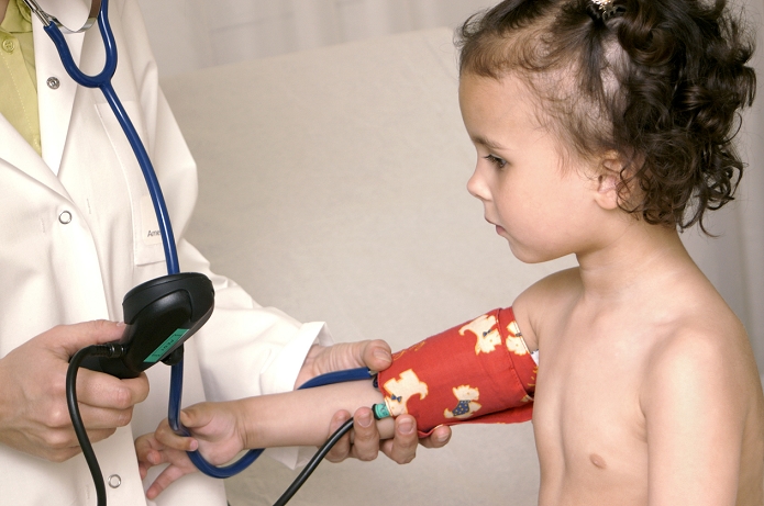 . Paediatric examination. Image 12 of 14. Doctor taking a young girl's blood pressure using a sphygmomanometer. A cuff is placed around the child's arm, which is inflated until the doctor can no longer hear blood flow through her stethoscope. The cuff is slowly deflated until blood flow is heard to resume. The pressure shown on the gauge (doctor's right hand) is the pressure of the pumping heart (systolic). Further deflation gives the pressure of the relaxed heart between pumps (diastolic). Blood pressure is measured in millimetres of mercury (mmHg). For a sequence of images showing a paediatric examination, see M825/831-843. MODEL RELEASED