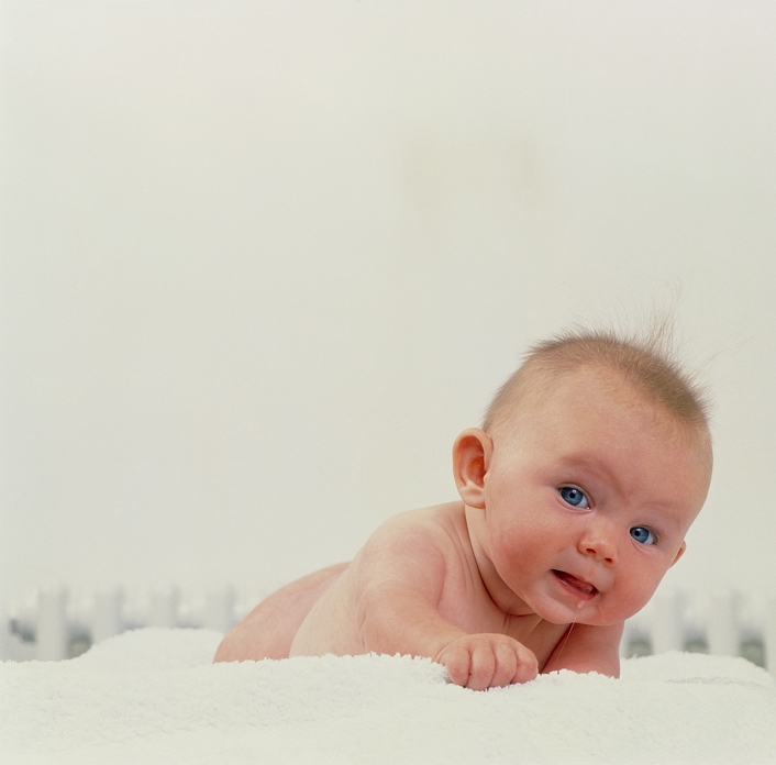 . Crawling baby. A naked, 4-month- old baby girl crawls along a white towel towards the camera. MODEL RELEASED