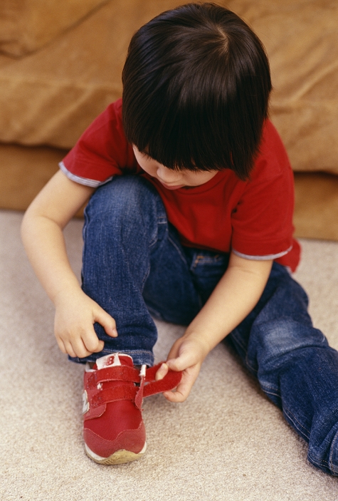 . A 3-year-old boy using a hooks and loops fastener while putting on his shoes. This can be helpful if children have not yet developed the dexterity to tie shoe laces. MODEL RELEASED