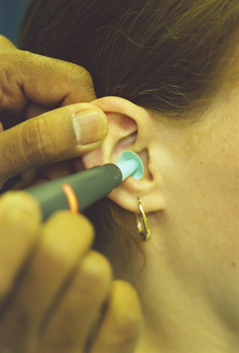 Tympanometry examination. Teenage girl having tympanometry to measure the movement of the eardrum (tympanic membrane) and assess the condition of the middle ear. A probe with an earplug (green) is inserted into the ear. A sound is emitted from the probe and, whilst the pressure in the ear canal is varied, the amount of sound reflected by the eardrum is recorded. The results are displayed on a tympanogram (not seen) which is interpreted by an audiologist. Tympanometry aids the diagnosis of glue ear (middle ear inflammation due to blockage of the Eustachian tube), which commonly affects hearing in children.