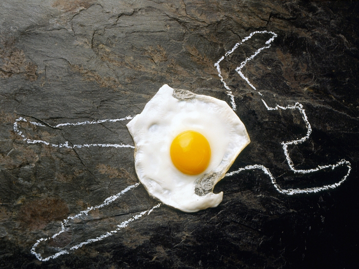 Death from cholesterol. Abstract image showing the white outline of a dead body on slate and a fried egg. It represents the role of fatty cholesterol- rich foods in disease of the heart and arteries. Too much fatty food can lead to obesity, and saturated fats such as found in eggs, cheese, red meat and other foods can raise blood cholesterol levels. Saturated fats in the form of low-density lipoproteins (a type of cholesterol) are a cause of atherosclerosis. Atherosclerosis is a disease where fatty deposits develop on the walls of blood vessels increasing the risk of coronary heart disease, heart attack, and stroke.