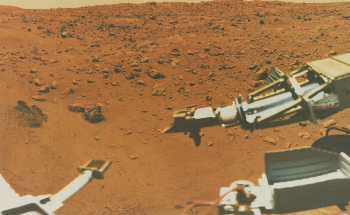 Viking 1 Lander picture of the region of Mars known as Chryse Planitia, the plains of gold, where the spacecraft set down on 20th July 1976. This picture was taken on the 15th August 1976 during the Martian summer. The scoop (right), in its parked position here, was used to dig a trench (left edge of picture) for obtaining samples of Martian soil from a debth of 30 centimetres (12 inches). The sky above the Martian horizon has an orange/brown cast caused by the suspension of dust particles in the atmosphere.