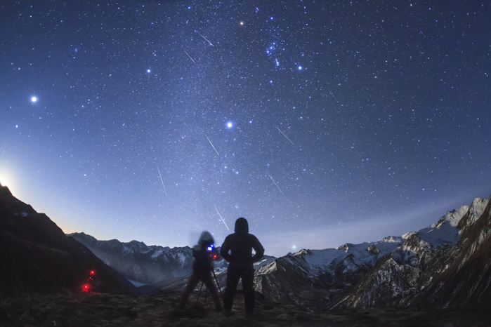 Geminid meteor shower over mountains in China Geminid meteor shower over mountains in China. Time exposure image of silhouetted human figures observing and photographing meteor trails in the night sky over snow capped mountains. The meteors are part of the annual Geminid meteor shower. The Geminids are a meteor shower that occurs annually in December. It is caused by debris from an object named 3200 Phaethon, thought to be an extinct comet. Visible in the night sky is Jupiter  far left , Sirius  centre , Orion  upper centre , and the faint band of the Milky Way  vertically above the photographer . The mountains are those around Mount Balang  5040 metres  in Sichuan, China, on the edge of the Tibetan Plateau. Photographed on 14 December 2014.