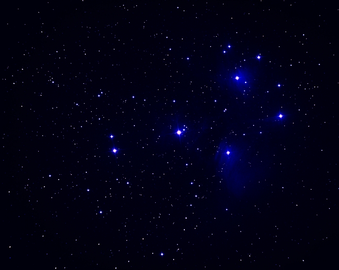 The Pleiades. Optical image of the Pleiades or Seven Sisters open star cluster (M45) which is situated in the constellation of Taurus at about 400 light years from Earth. The Pleiades cluster is relatively young, being about 50 million years old. It is still embedded in a cloud of cold gas and interstellar dust, seen here as a blue nebulosity, which is the material left over from the cluster formation. The cloud forms the finest and nearest example of a reflection nebula and appears blue because blue light is reflected more efficiently by the interstellar particles. Despite its common name, up to 12 of this star cluster's stars are visible to the naked eye.