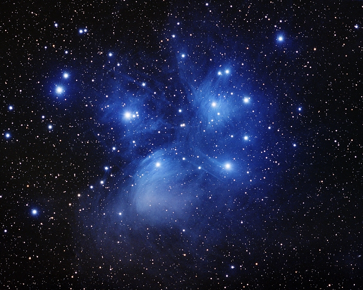 Pleiades star cluster, optical image. This cluster (M45) comprises over 3000 stars. All the stars formed at around the same time. They are young by stellar standards, around 100 million years old. The stars are wreathed in blue nebulosity. This is a reflection nebula, a cloud of dust that reflects the blue light of the stars. It was thought that the nebula was the vestiges of the matter from which the stars formed, but modern measurements have shown that the cloud is passing through the cluster purely by chance. The Pleiades cluster lies around 400 light years from Earth in the constellation Taurus.