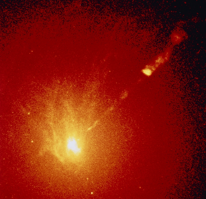 The core and optical jet of galaxy M87. Coloured optical image of the centre of M87 made by the Hubble Space Telescope (HST). M87 is a large elliptical galaxy with an active core. The very centre of the core has a far stronger gravitational field than explainable by the observed stellar density, suggesting the presence of a supermassive black hole. This black hole is also presumed to be the 'engine' which powers the optical jet seen here pointing toward upper right. The jet consists in visible light emitted by a cone of fast-moving electrons as they spiral through the galaxy's immense magnetic field.