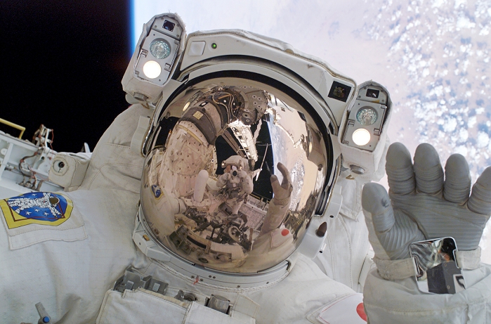Return to Flight spacewalk. Astronaut Soichi Noglichi (from Japan's space agency) waving for the camera. Astronaut Steve Robinson is seen taking the picture reflected in the visor. This was taken during the second spacewalk while space shuttle Discovery was docked to the International Space Station (ISS). During the 7 hour spacewalk the astronauts replaced 1 of the 4 gyroscopes that maintain the ISS's orientation in space. This mission, Return to Flight or STS-114, launched on 26th July 2005. It was the first shuttle mission since Columbia was lost on re-entry on 1st February 2003. Photographed on 1 August 2005.