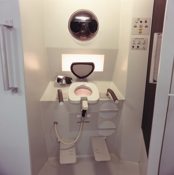 Astronaut comfort. The lavatory in the mock-up of the Freedom Space Station. Disposal of urine and faeces becomes quite a problem in weightlessness. Suction fans are used to ensure that solid and fluid waste are collected efficiently, either in the bowl (centre) or in the urinal (fixture on pipe). Foot restraints and hand-holds are also provided. The waste is collected in a disposable container where it is dried and compacted to minimise storage volume. Hands may be washed in the device at top. The compartment is fitted with a sliding door to ensure privacy. Freedom is scheduled for completion and permanent occupation by mid-1999.