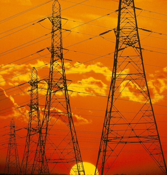 Electricity pylons. Electricity pylons carrying high voltage wires against a background of the setting sun. The wires have to be high above the ground to prevent them interfering with land-based objects. The wires carry electricity from power stations to substations in towns and cities.