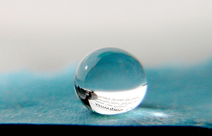 Water repellent surface. Close up of a water droplet resting on a water-repellent coated surface. The coating contains inorganic nanoparticles that increase the contact angle between the surface and water. The larger the contact angle, the more hydrophobic (water repellent) the surface becomes, until the water droplet forms a near-spherical shape which collects dirt as it rolls off the surface. This self-cleaning and waterproof property is known as the 'lotus effect,' and is named after the same properties found on the lotus leaf. Materials covered with this coating are able to withstand corrosion and maintain a clean surface. Photographed by Seashell Technology for the US Airforce, USA.