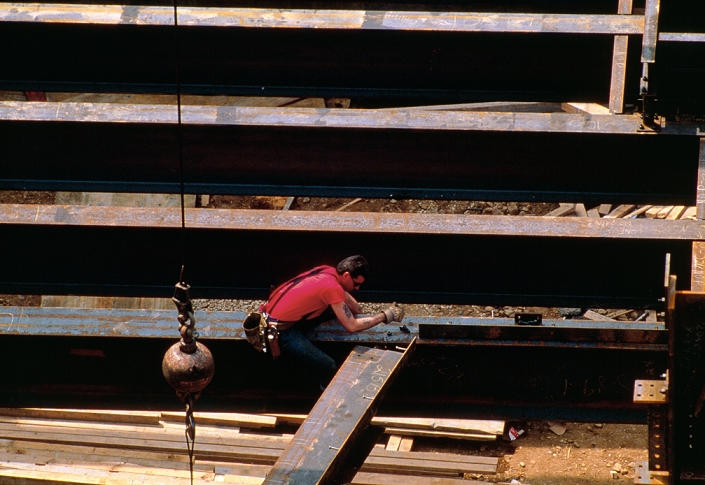 Building construction site. View of a building under construction, with a workman sitting ontop of and securing steel girders.