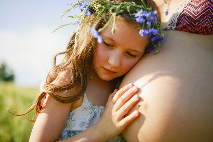 Serene girl with flowers in hair leaning on pregnant mothers stomach