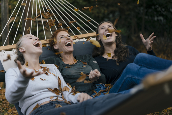 Carefree mother with two teenage girls throwing autumn leaves in hammock in garden Carefree mother with two teenage girls throwing autumn leaves in hammock in garden