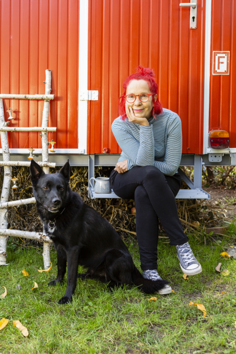 Portrait of content senior woman with red dyed hair sitting in front of red trailer in the garden with her dog Portrait of content senior woman with red dyed hair sitting in front of red trailer in the garden with her dog