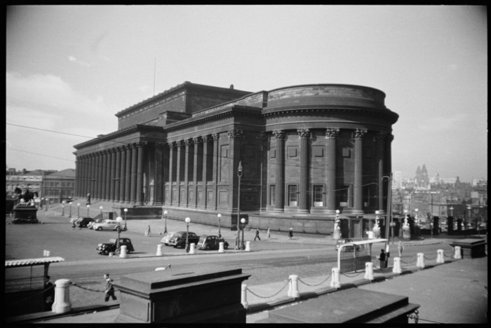 St George s Hall, Liverpool, Merseyside, c1955 c1980. Creator: Ursula Clark. St George s Hall, Liverpool, Merseyside, c1955 c1980. A view of the north and east front of St George s Hall, seen from the north. St George s Hall is a large classically inspired building, designed by Harvey Lonsdale Elmes and Charles Cockerell and built between 1841 and 1856 to be used as a public hall and law courts. The north end in the foreground has a semi circular projection with nine bays separated by fluted corinthian columns. The top section of the bays have embedded square plaques, and the lower section sash windows. To the left is the east front, with a six bay loggia with corinthian columns, and square plaques with relief carvings of figures, and further right is the entrance. The entrance consists of a free standing arcade of sixteen fluted columns at the top of the platform accessed by a large flight of steps. In front of the hall is a bronze statue of Benjamin Disraeli, made in 1886 and located in the middle of the steps to the hall. Further east fom the steps is bronze equestrian statue on a stone plinth, by Thomas Thorneycroft and dated 1870. There is also a car park and pedestrians on St George s Plateau, and in the background is a view of Liverpool, looking west.